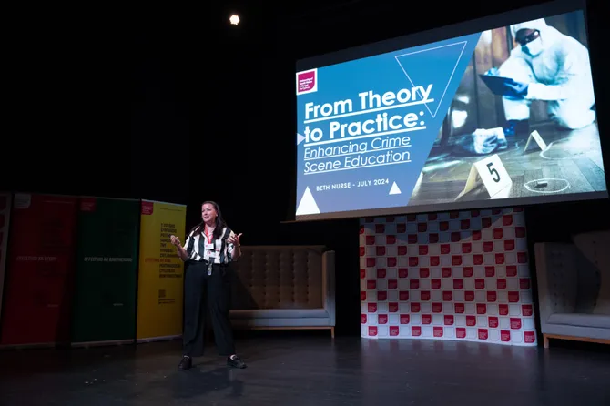A person presenting on stage. The presentation behind them reads 'From Theory to Practice: Enhancing Crime Scene Education