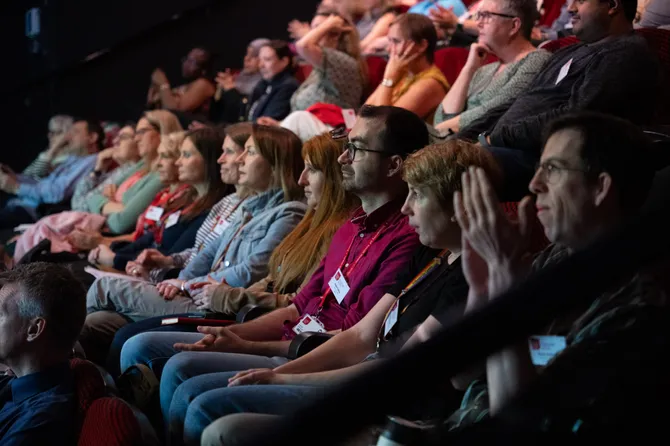 An audience listening to a conference speaker in a lecture theatre.