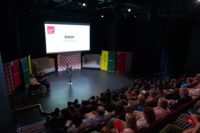 A lecture theatre full of conference attendees listening to a speaker on the stage.