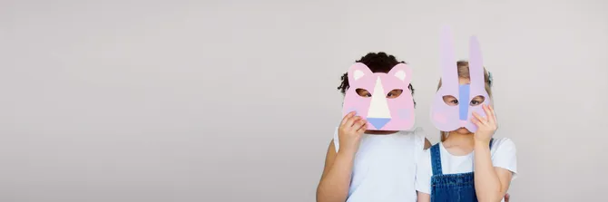 Two children holding up handmade animal masks to their faces