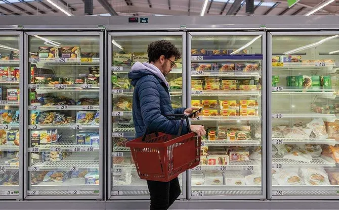 A person shopping in a supermarket and reading the packet of something from the freezer.