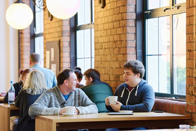A father and son sat in Ty Crawshays cafe on the USW Treforest campus. They are smiling and talking over a cup of coffee.