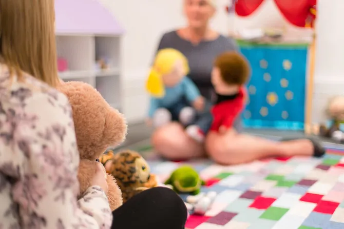 A woman is performing a puppet show for a young girl holding a teddy.