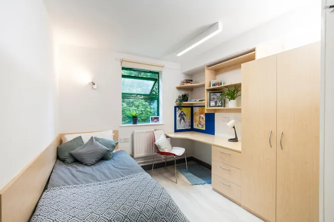 A single room at our Pontypridd accommodation featuring a bed, desk, window and wardrobe.
