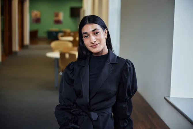 Business and Management student, Samaya Khan, is sat in the postgraduate centre, smiling at the camera.