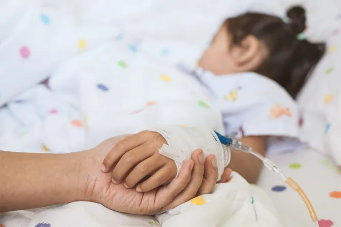 Parent holding the hand of a child who is sleeping in a hospital bed