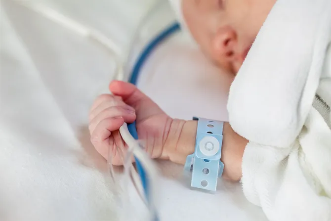 Close up image of a newborn baby holding on to wires in an incubator