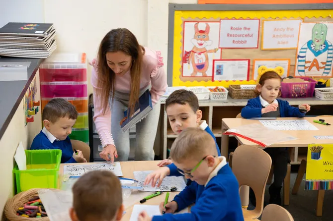 A student teacher interacting with students in a colourful primary school classrom.
