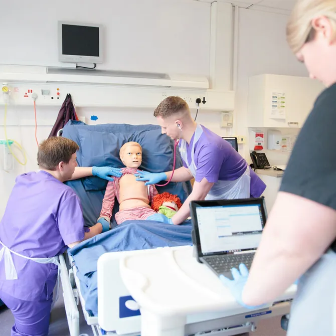 Two student nurses treating a dummy in the clinical simulation suite, whilst being observed by a lecturer