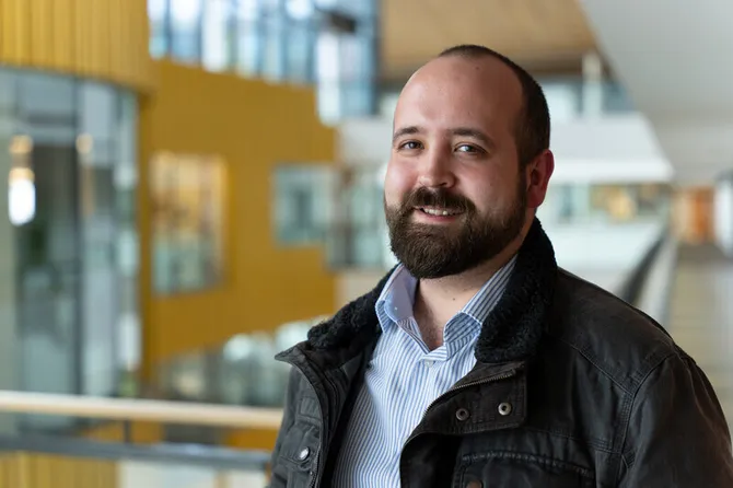 A man stood in the corridor of the Newport campus, smiling at the camera.