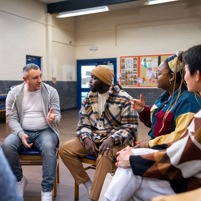 A youth worker and young people sat on chairs in a circle chatting