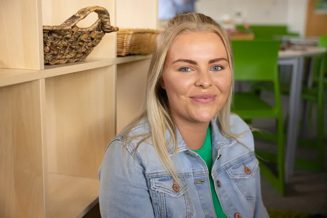 A close-up of a student smiling while sat on the floor with a simulation primary school classroom behind them at Treforest campus