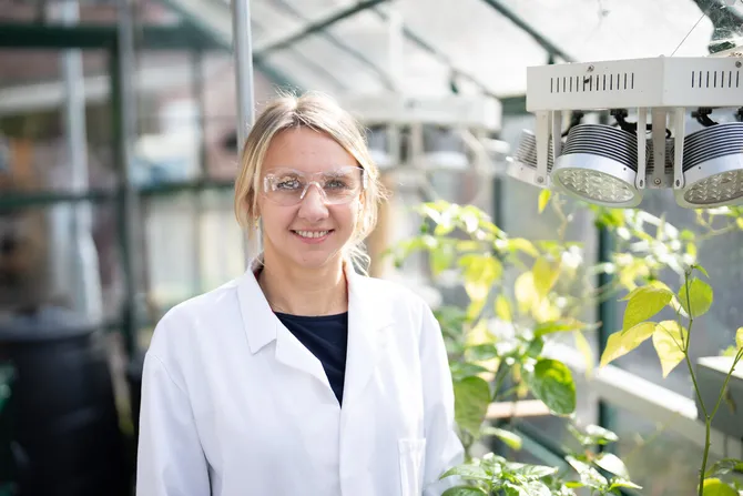 dr martha ragu standing in greenhouse next to plants from phd studies