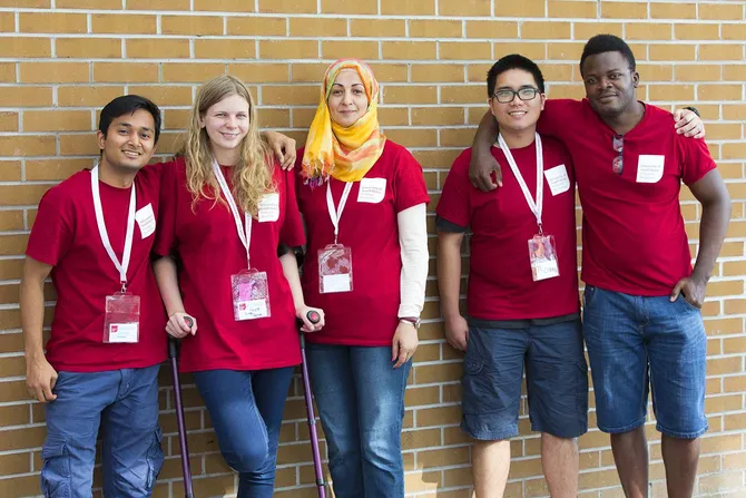 A group of people wearing red USW tshirts are stood together, smiling against a brick wall.