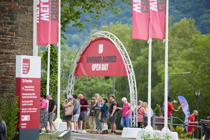 Long shot of a queue of prospective students and their family walking under the open day archway banner at Treforest Open Day
