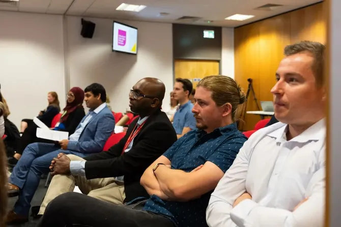 7 postgraduate research students sat in a conference setting listening to presentation