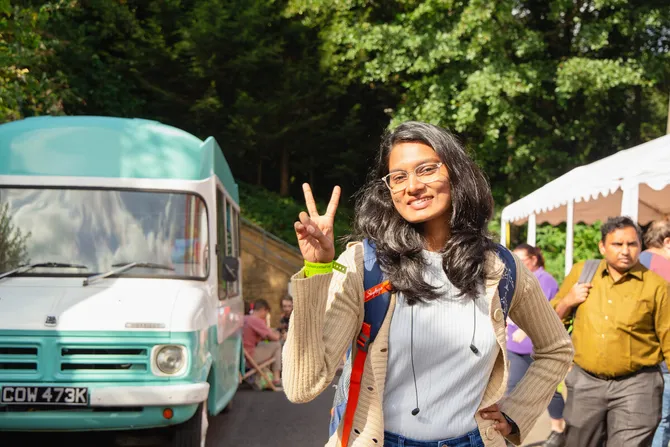 Student smiling and giving a peace sign with food trucks in the background at Treforest Welcome Fest