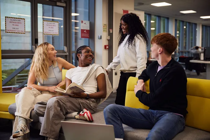 Four students sat on sofas smiling and studying in the library.