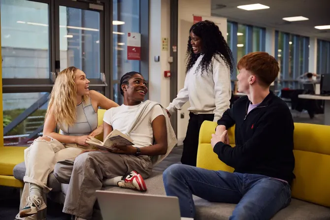 Four students sat on sofas smiling and studying in the library.