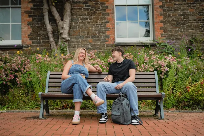 Two students sat on a bench chatting and smiling outside Crawshay's