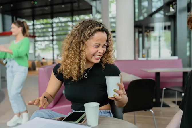 Close up image of a student smiling and laughing whilst enjoying a coffee at Newport campus