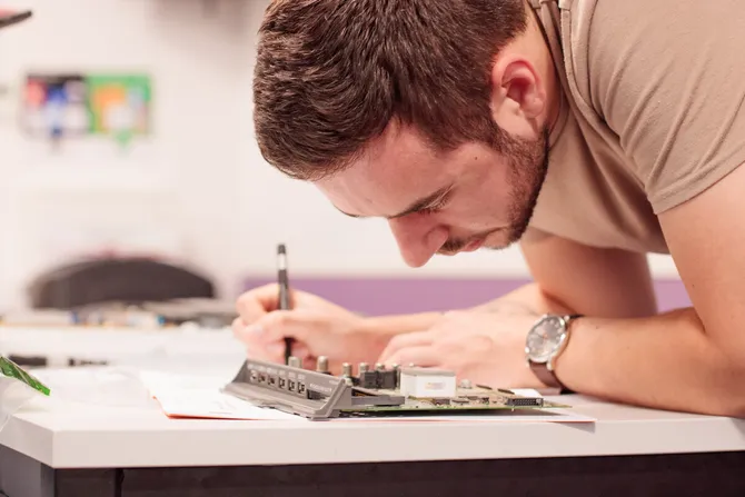 student holding pen, looking at electronic equipment