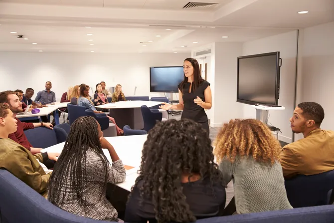 teacher standing at the front of a higher education class talking to students