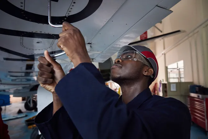 A student is standing under the wing of a plane unscrewing some bolts.