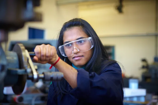 A student is focusing on a peice of machinery, they are wearing eye protection glasses.