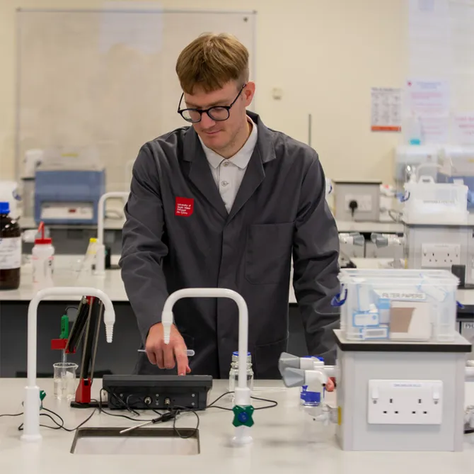 a student in USW overalls conducts an experiment involving electronic equipment in a laboratory