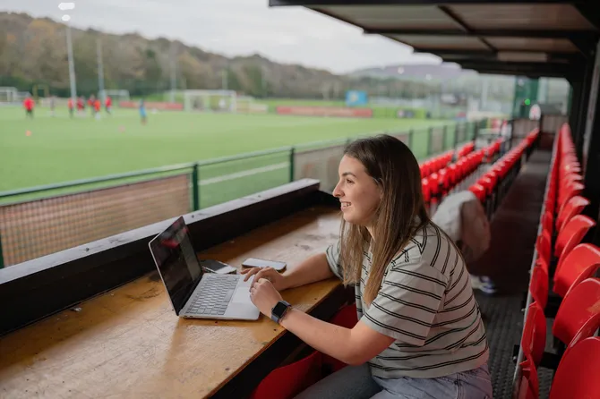 Sport Journalism student Leah Bower sat in a sport stand reporting on a sporting game
