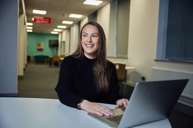 Marketing student Chloe Buckley sat at a desk with a laptop smiling off camera