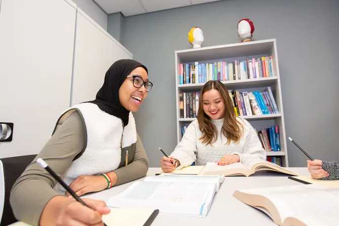 Two psychology students studying at a desk surrounded by books and psychology equipment