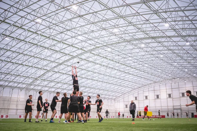 Students are playing rugby on the indoor 3g pitch, they are lifting someone to catch the ball.