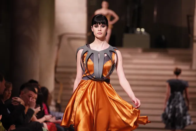 A model walking down a catwalk in a bright orange dress