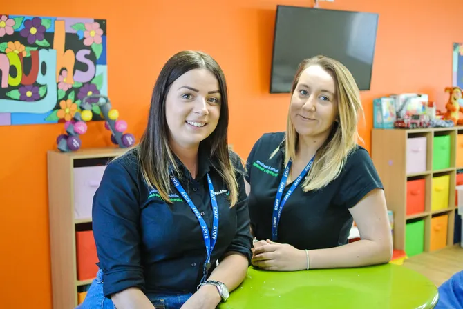 Two students stood next to each other smiling into camera. They are on placement.