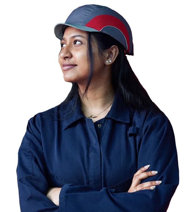 An engineering student in overalls and a helmet with her arms crossed looking away from the camera