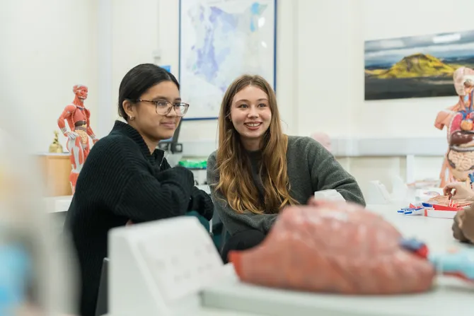 Two students smile while listening in a medical science laboratory in Glyntaff while surrounded by medical anatomy models