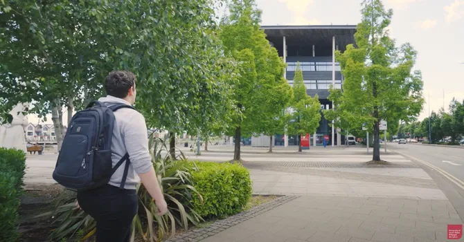 student walking towards the newport campus wearing a rucksack and grey jumper