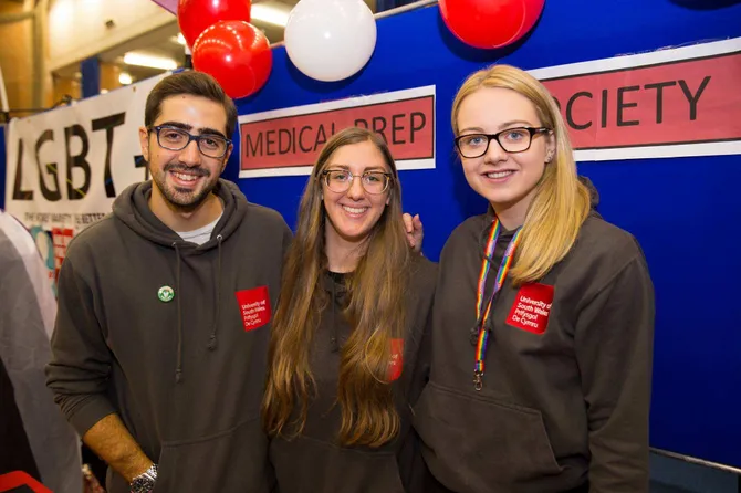 three members of the medical preparation society smiling to the camera wearing grey US hoodies