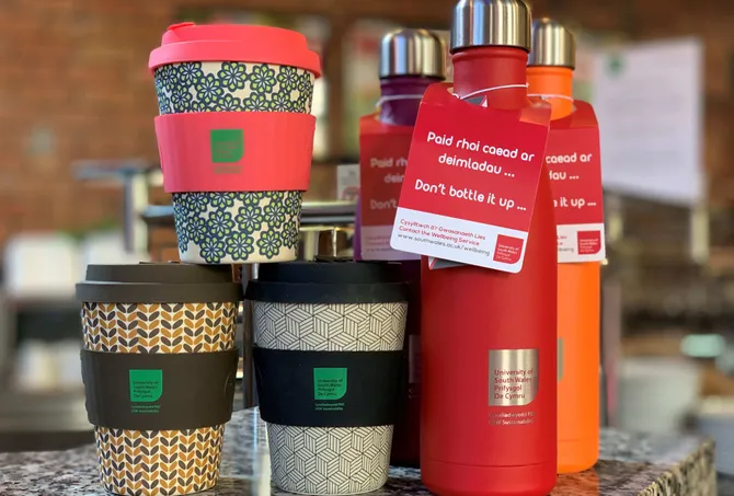 A collection of USW branded reusable coffee cups and water bottles