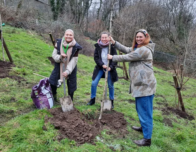 A group of people smile proudly at the camera after planting a tree