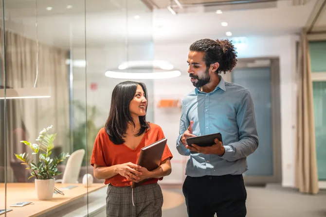 Two colleagues walking through an office together talking.