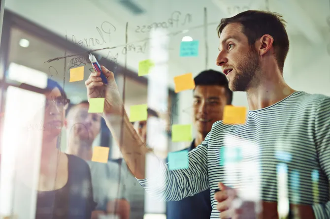 A team brainstorming with pens and post-it notes on a clear whiteboard.