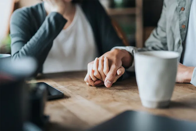 Close up image of two people holding hands on a table with a coffee cup to the side