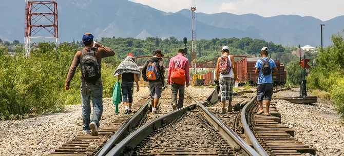 A group of refugees walking together along railroad tracks,
