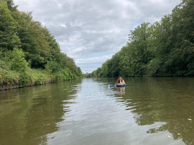 PhD Theatre and Performance student, Lucy, lying on a paddle on a board and smiling at camera