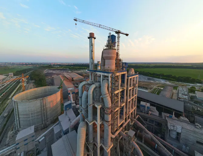 Cement plant with high factory structure and tower cranes at industrial production area. Manufacture and global industry concept.