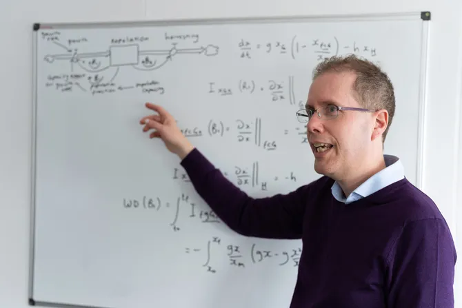 Professor Paul Roach speaks while pointing at an equation written in marker on a white board