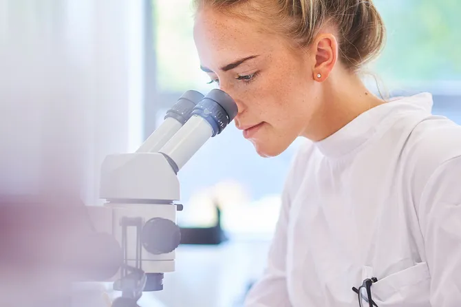A research scientist is analysing a sample on her microscope in a microbiology lab